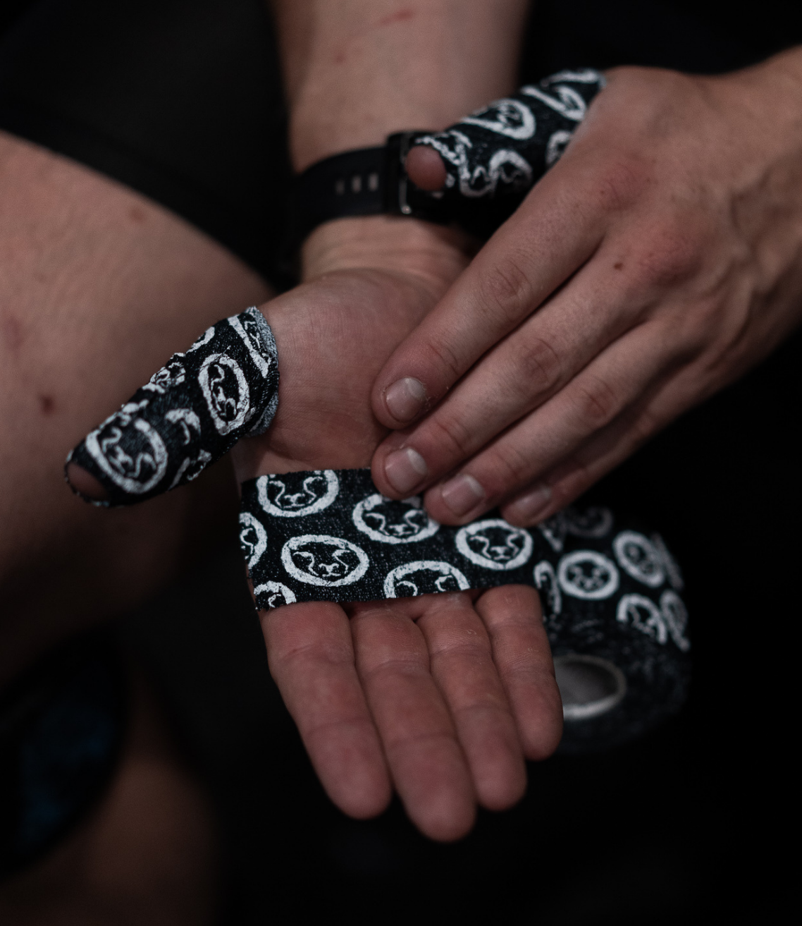 Close-up of hands wearing black Mammal Tape on a dark background